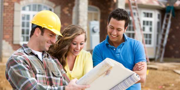 two homeowners and a builder smiling while looking at blueprints