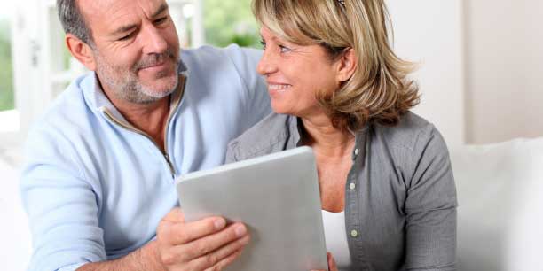 an older couple smiling while looking at a tablet